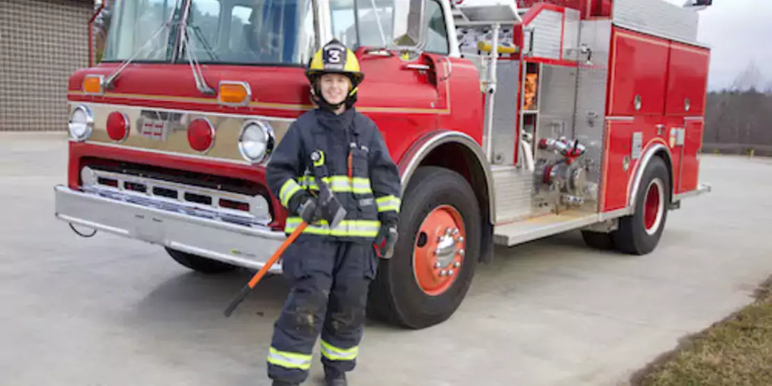 Young female firefighter with an axe standing in front of a fire truck